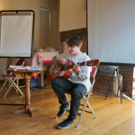 A young performer is sat down playing guitar and singing